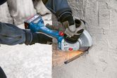 A person wearing safety equipment uses an angle grinder to cut a rebar in concrete.