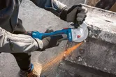 A person wearing safety equipment grinds concrete, producing sparks with an angle grinder.