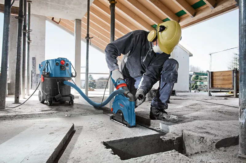 A person wearing safety equipment cuts a groove into concrete, connected to a wet/dry extractor.