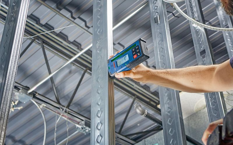 A person uses a laser receiver to align metal studs in a construction frame.