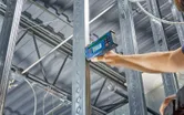 A person uses a laser receiver to align metal studs in a construction frame.