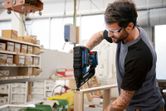 A person wearing safety equipment uses a cordless wood nailer to assemble furniture.