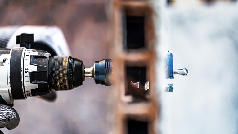 A person wearing safety equipment drills through a brick wall.