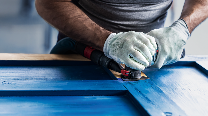 Person wearing safety equipment sands a blue wooden surface with a power tool.