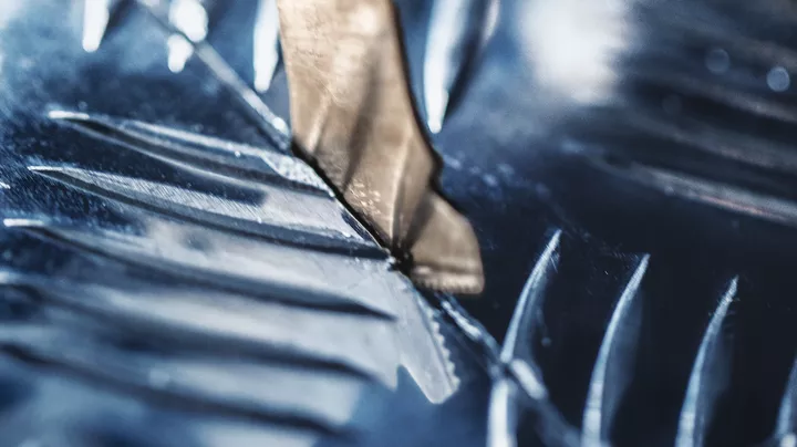 Metal drill bit cutting through a shiny metal surface.