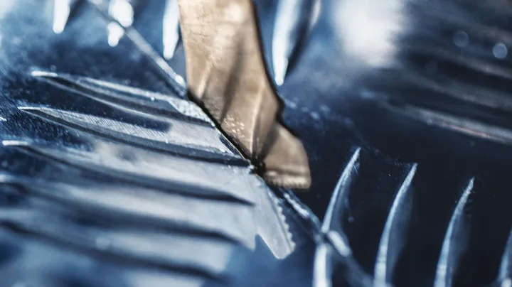 Metal drill bit cutting through a shiny metal surface.