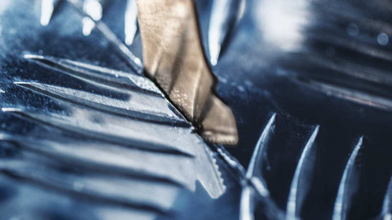 Metal drill bit cutting through a shiny metal surface.