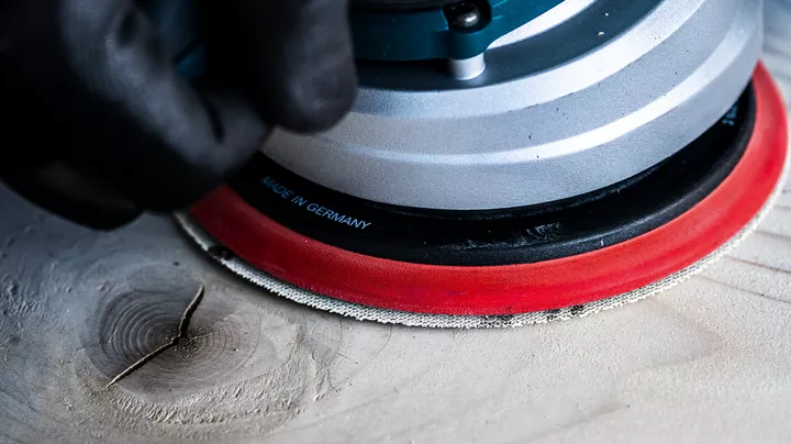 Person wearing safety equipment sanding a wooden surface with a power tool.