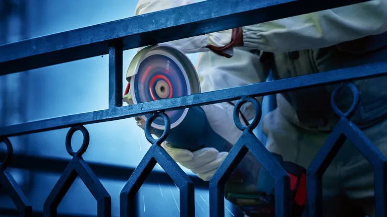 A person wearing safety equipment grinds a metal fence with a power tool.