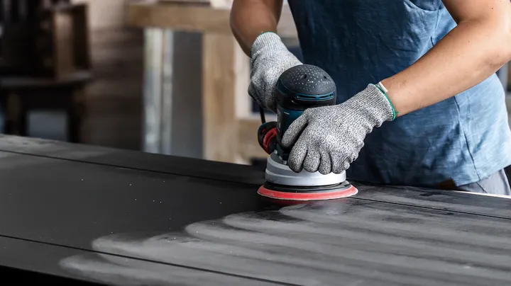 Person wearing safety equipment sands a wooden surface with a power sander.