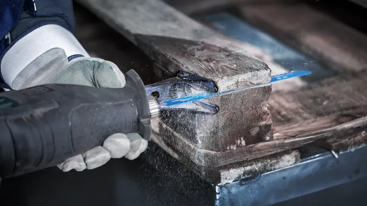 Person wearing safety equipment uses a reciprocating saw to cut through a wooden pallet.