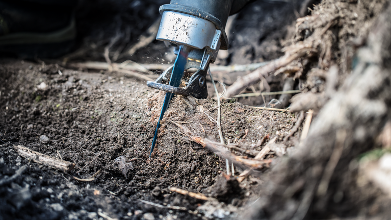 Reciprocating saw cutting through a tree root in the soil.
