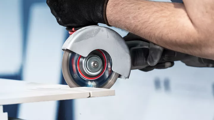 Person wearing safety equipment cuts tile using a handheld circular saw.