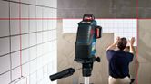 Laser leveling tool projects red lines as a person installs tiles on a wall.