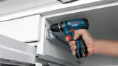A person grips a compact cordless drill in their right hand.