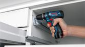 A person uses a cordless drill driver to fasten a screw in a cabinet frame.
