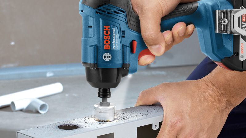 A person drills a hole in metal using a cordless power tool.