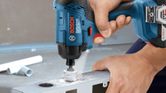 A person drills a hole in metal using a cordless power tool.