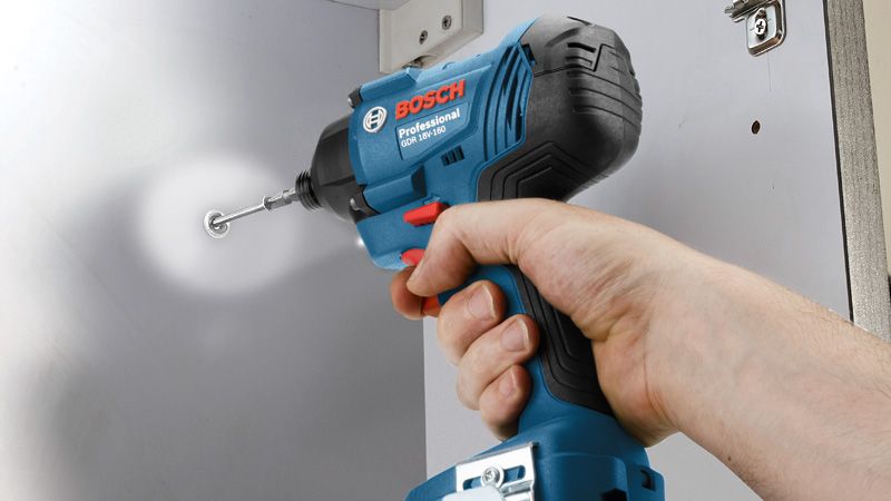A person uses a cordless impact driver to fasten a screw into a cabinet.