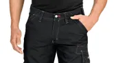 A person stands wearing black trousers with knee pockets.