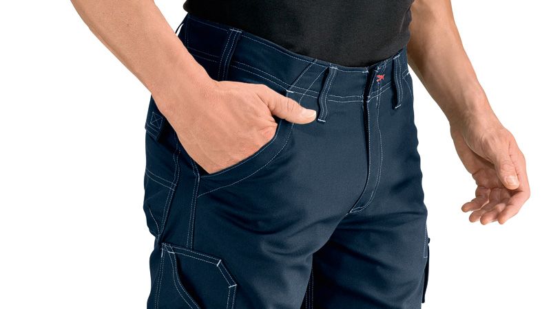 Person wearing blue work trousers with knee pockets, hand resting in front pocket.