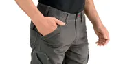 Person wearing grey trousers with knee pockets, one hand in pocket.
