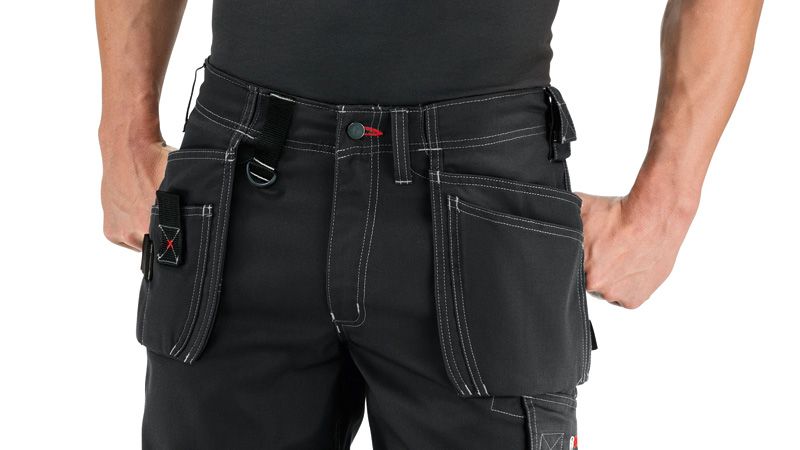 A person wearing black shorts with holster pockets stands with hands in pockets.
