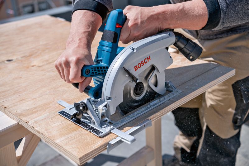 A person cuts plywood with a cordless circular saw.