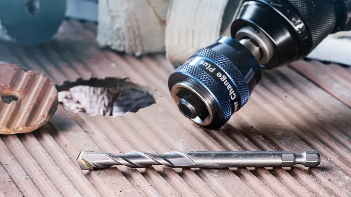 Drill and bit placed on a grooved tile surface next to a freshly made hole.