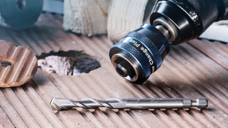 Drill and bit placed on a grooved tile surface next to a freshly made hole.