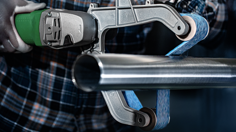 Person wearing safety equipment polishes a metal pipe with a belt grinder.