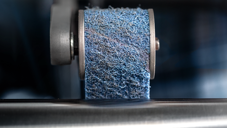 A blue abrasive wheel polishes a metal surface.