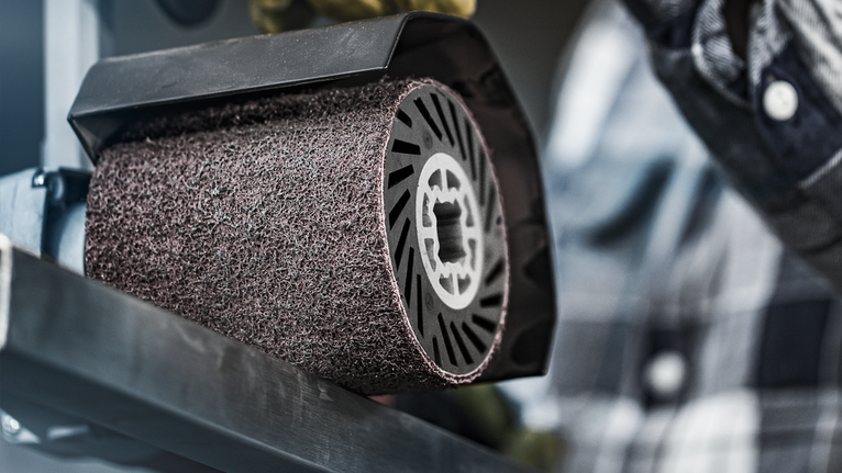 A person operates a power tool with a large abrasive wheel on a metal surface.