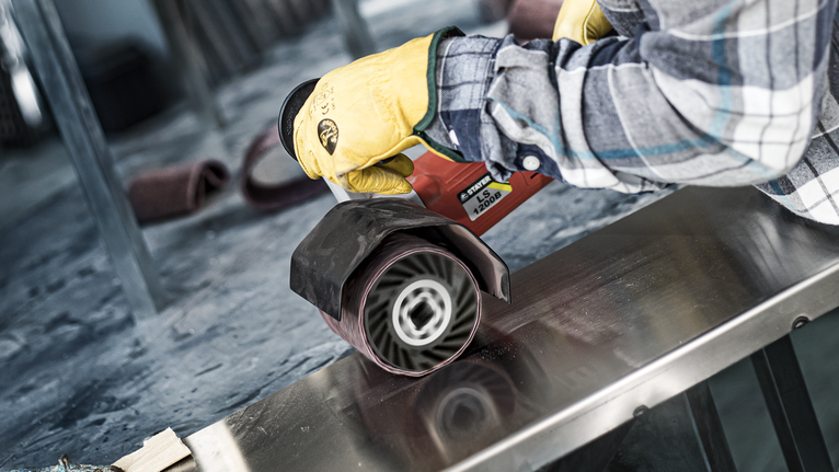 A person wearing safety equipment polishes a metal surface using a power tool.