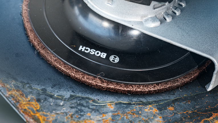 Angle grinder with abrasive disc smoothing the edge of a rusty metal surface.