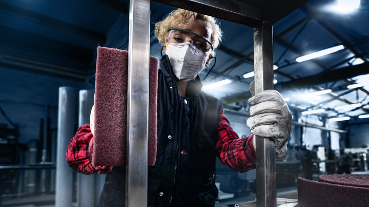 Person wearing safety equipment polishes a metal frame with a sanding block.