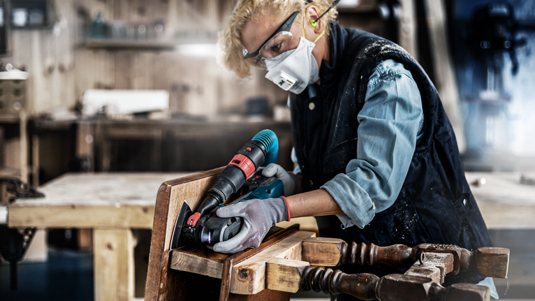 A person wearing safety equipment drills into wood using a power tool.