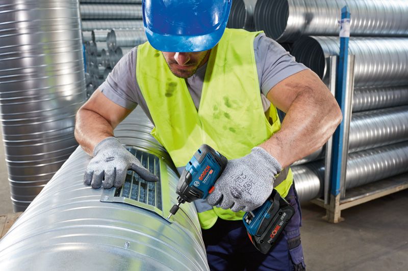 A person wearing safety equipment fastens a vent cover onto a large metal duct.