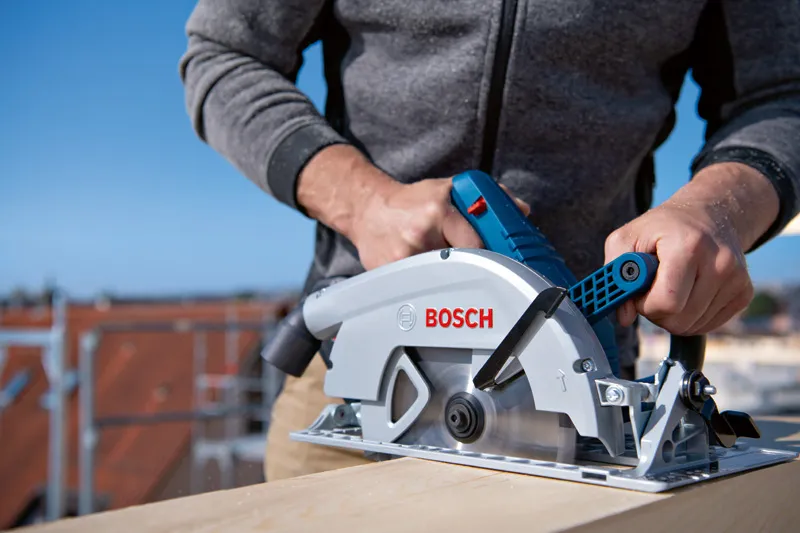 A person cuts wood outdoors using a cordless circular saw.