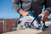 A person cuts wood outdoors using a cordless circular saw.
