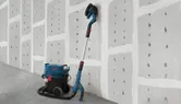 Drywall sander connected to a dust extractor resting against a finished wall.