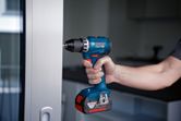 A person uses a cordless drill to screw into a door frame.