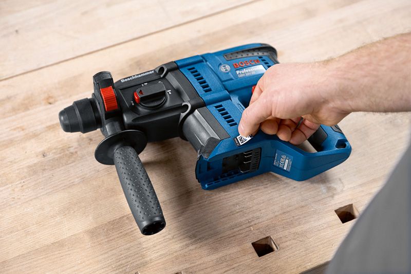 Person adjusts a blue rotary hammer drill resting on a wooden workbench.