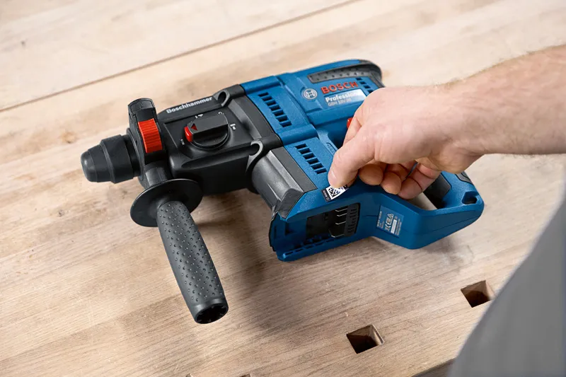 Person adjusts a blue rotary hammer drill resting on a wooden workbench.