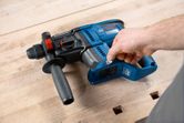 Person adjusts a blue rotary hammer drill resting on a wooden workbench.