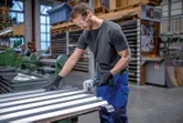 A person wearing safety equipment cuts sheet metal with a cordless nibbler in a workshop.