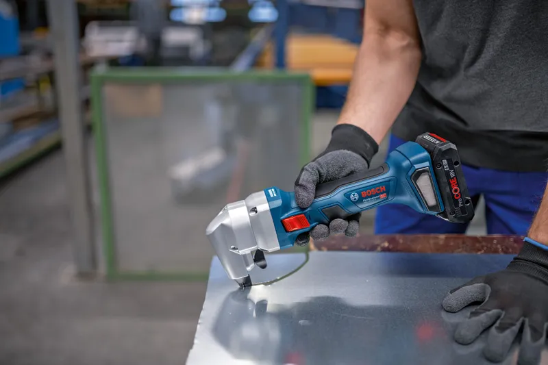 A person wearing safety equipment cuts sheet metal with a cordless nibbler.