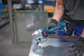 A person wearing safety equipment cuts sheet metal with a cordless nibbler.