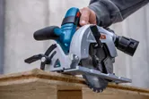 A person cuts wood with a circular saw on a construction site.