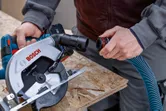 Person attaches a vacuum hose to a circular saw on a wooden board.